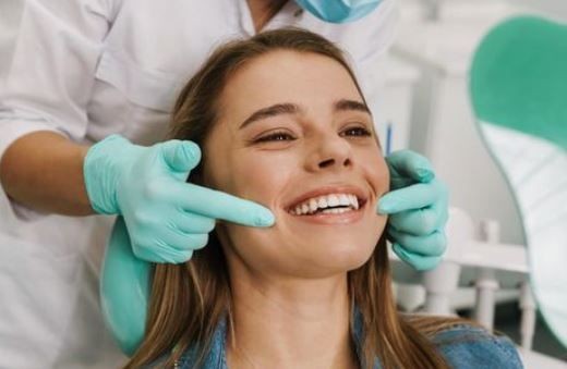 Dentist wearing gloves examining a smiling patient's teeth in a dental chair.