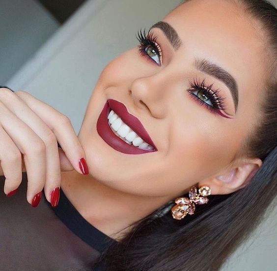 Woman wearing pink gemstone earrings and red nail polish, with hand resting on her chin.