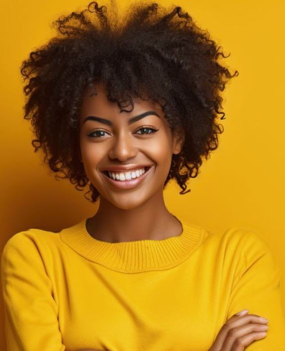 Person with curly hair wearing a yellow sweater, standing against a yellow background.