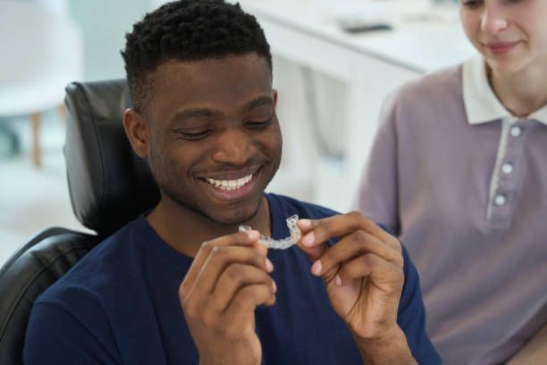 Person holding a clear dental aligner in their hands, seated indoors.